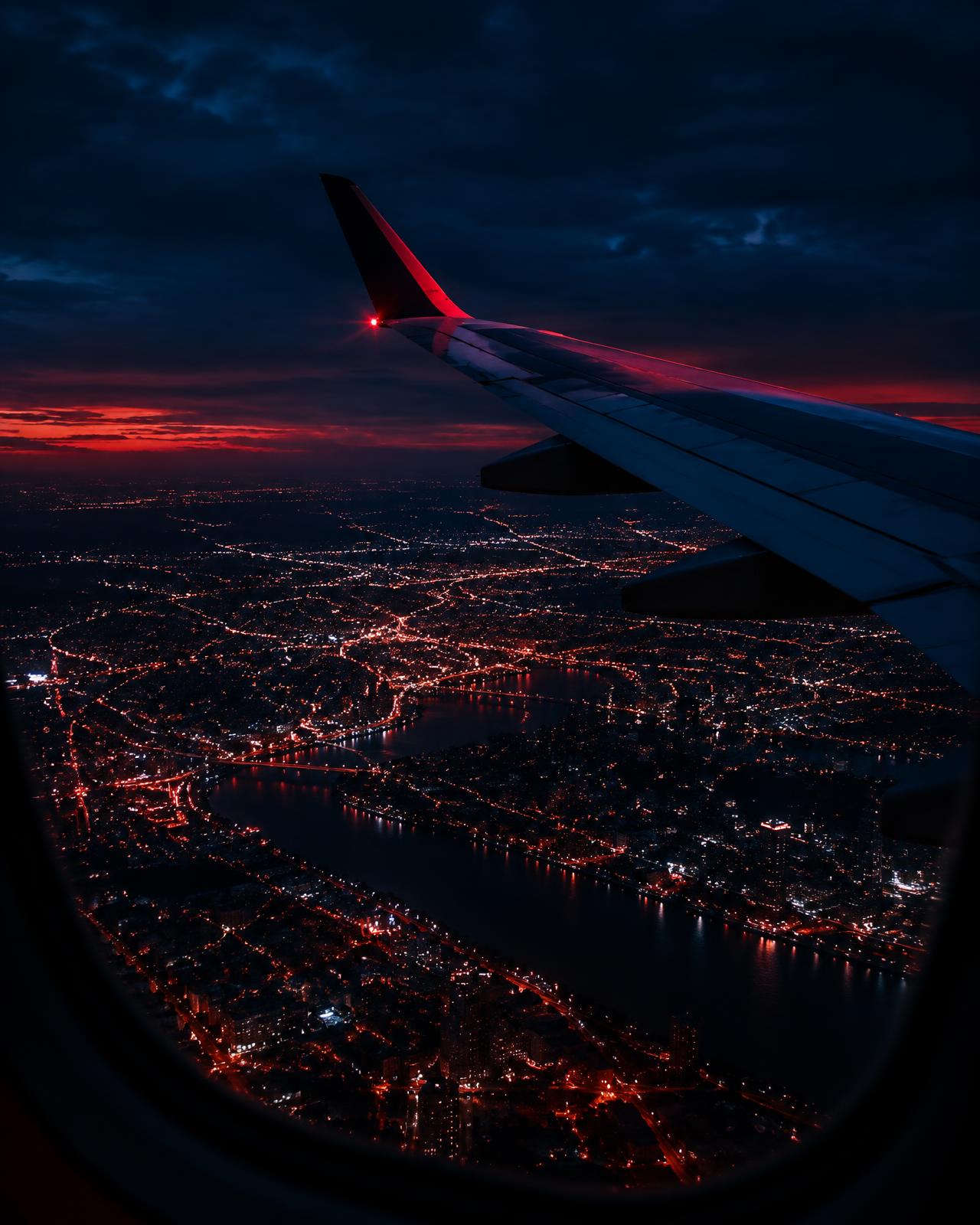 Blick aus dem Flugzeugfenster auf eine beleuchtete Stadt bei Nacht